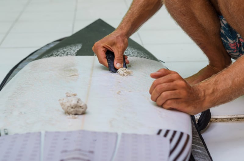 removing old wax from surfboard with a scrapper